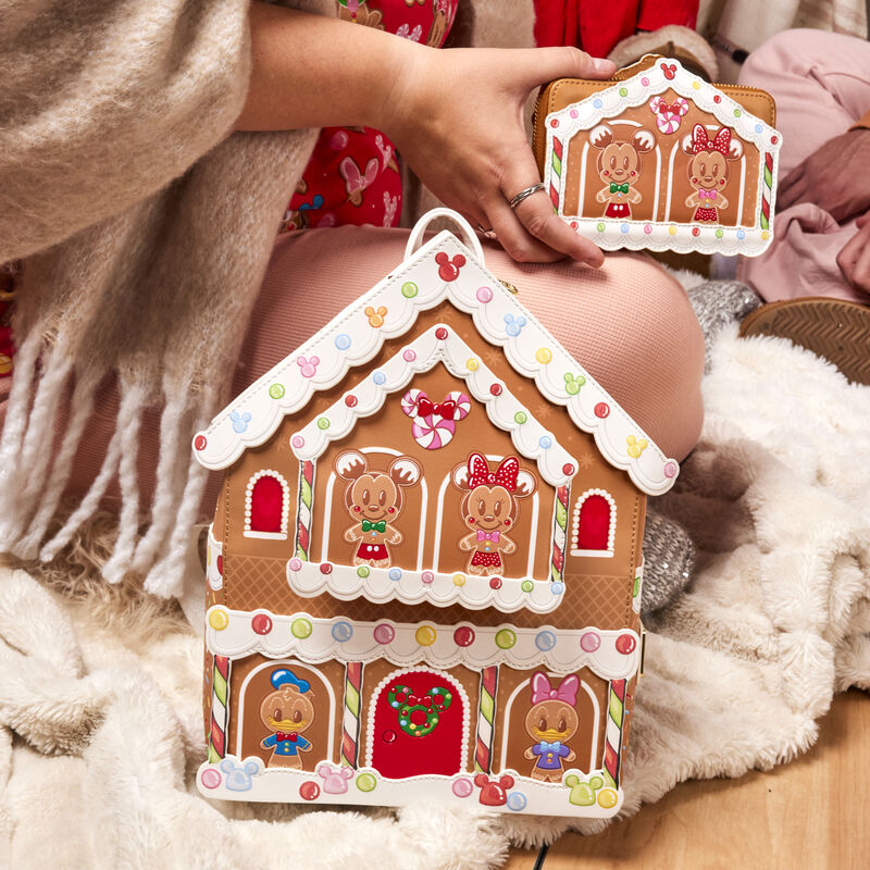 Image of someone sitting on the floor, our gingerbread house mini backpack resting against their leg and they're holding the matching gingerbread house wallet